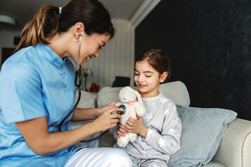 Smiling girl sitting on sofa and holding her bunny toy. Doctor trying to relax girl so she is...