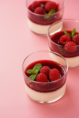 Italian dairy dessert panna cotta with raspberry jam, fresh raspberries and mint on pink surface