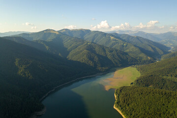 Aerial view of big lake with clear blue water between high mountain hills covered with dense evergreen forest