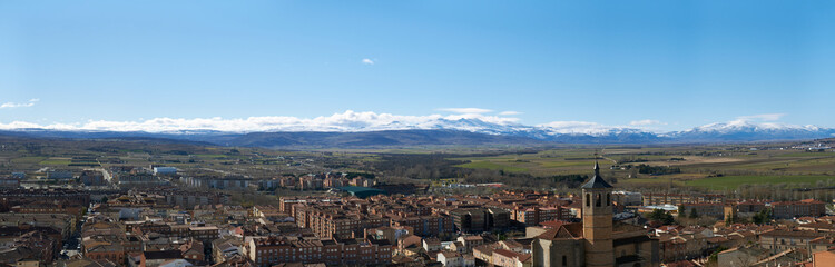 Fototapeta na wymiar Panoramic view of South West part of the city in Avila, Spain. The St. Nicholas Church in the foreground and the Sierra de Gredos mountain range covered with snow in the background.