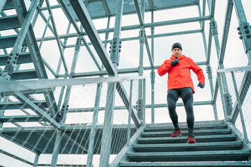 Smiling runner man dressed bright red softshell sporty clothes running down by huge steel industrial stairs in cold winter day. People healthy lifestyle concept photo.
