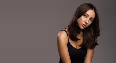 Fototapeta premium Hair or skin care concept. Portrait of a luxurious young woman with healthy hair and skin on studio gray background free space for text