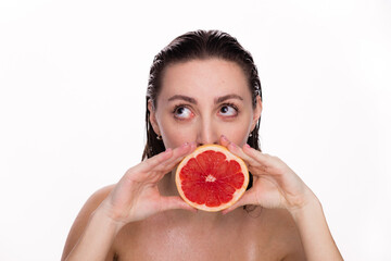 Happy young beautiful woman with healthy glow perfect smooth and wet skin holds piece of red grapefruit near face. Natural cosmetics, skincare, wellness, facial treatment, cosmetology, diet concept.