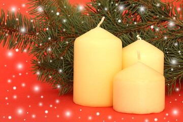 Three candles stand against the background of fir branches. Christmas theme.