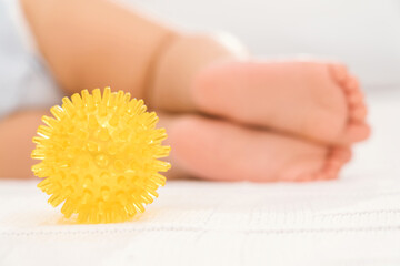 A yellow massage ball and the legs of a sleeping baby in the background. Selective focus. The...