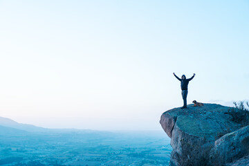 person on the top of the mountain with open arms and his dog happy