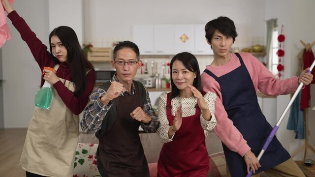slow motion of energetic asian father. mother. daughter and son in aprons looking at camera while making kung fu pose with cleaning supplies at home kitchen background. ready for spring cleaning