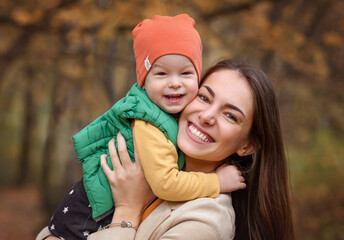 Fototapeta premium little boy in a green jacket and jeans orange hat hugs hugs mom in the park in autumn