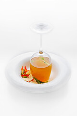 Restaurant serving of soup 1 - a glass of broth is turned upside down on a plate, next to it are vegetables and slices of white fish. Insulated Food Dish