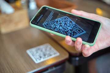 Closeup of guest hand ordering meal in restaurant while scanning qr code with mobile phone for...