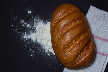 Bread on flour on a black background. Bakery product. Freshly baked loaf