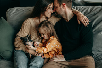 Mom, dad, daughter and dog are sitting at home on the couch and hugging each other