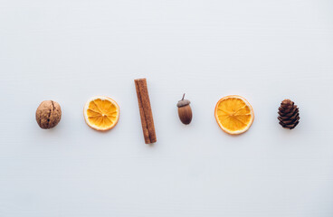 Holiday flat lay with natural decorations such as pine cones, cinnamon sticks, dry orange slices, acorns and walnuts on white wooden background. Zero waste Christmas concept. Plastic free holidays. 