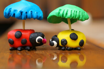 Figurines of two ladybirds with umbrellas made of plasticine.
