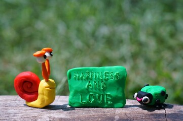 Toy snail and ladybug made of plasticine close-up. Next to it is the inscription happiness and love.
