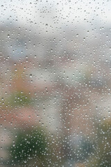 rain drops on windowpane over blurred city view with buildings or houses