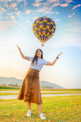 A woman standing on the green grass and happily take a picture with a hot air balloon