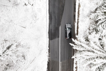Aerial birds-eye view of a car in motion, panning shot from a drone. Amazing road in the middle of a forest in winter landscape.