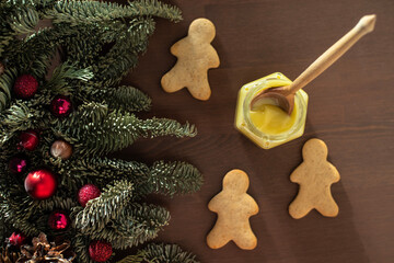 on a wooden table with Christmas branches, a jar of honey with a spoon and three gingerbread men . spicy ginger cookies and nobilis decorated with Christmas tree toys on the table. New Year's pastries