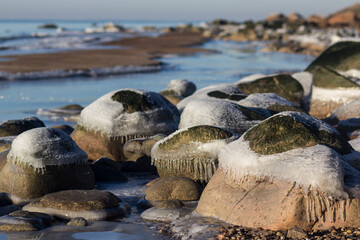 Winter landscape with ice and stones on frozen Sea. Ice frozen on a stone. Sea shore in winter, covered with ice and snow