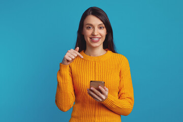 Joyous caucasian female with big smile, pointing at smartphone, rejoices having new app, enjoys...