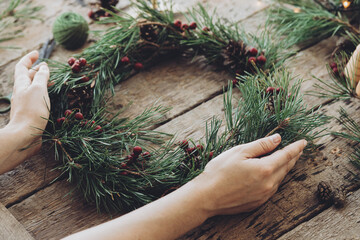 Woman holding handmade Christmas wreath on a wooden table, Advent celebration wreath with pinecones and red berries made during Christmas workshop