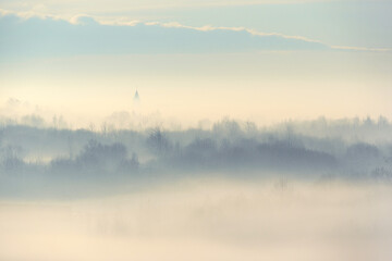 Fototapeta na wymiar Outlines of trees and church in the fog creeping. Winter landscape