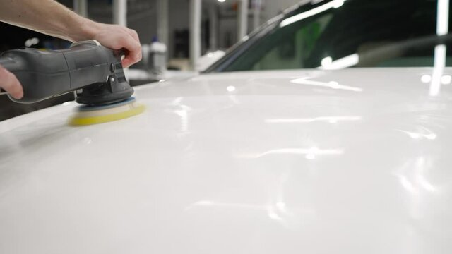 The foreman on the palletizer cleans the machine. Car detailing - Car care service. Man holding a polisher in his hand. Car polishing process.