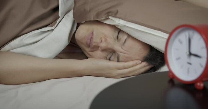 Situation for sleeping. A woman with a pillow on her head has an insomnia because of loudly sounds in the room.