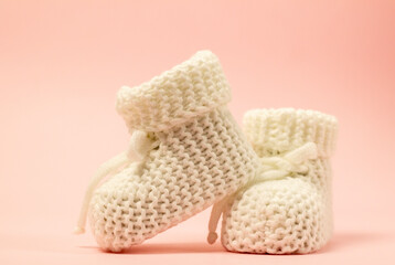 Crochet white baby booties, on a pink background, handmade baby booties, warm baby feet is a guarantee of health. space for text