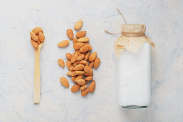 Almond milk in a bottle with a handful of seeds and a wooden spoon on a light background.