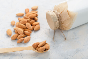 Almond milk in a bottle with a handful of seeds and a wooden spoon on a light background.