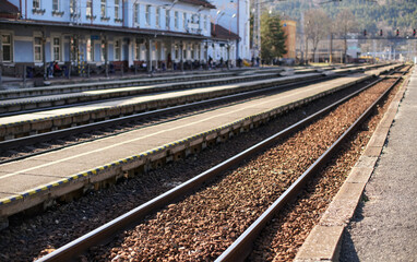 Obraz premium Train station in small city on sunny day, shallow depth of field photo, focus on concrete platform and steel rail foreground