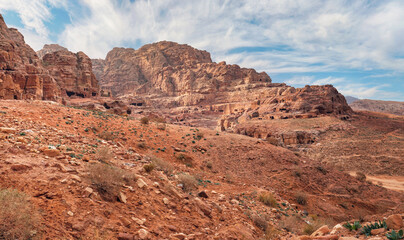 Fototapeta na wymiar Typical landscape at Petra, Jordan, red dusty ground, mountains with carved buildings inside in distance