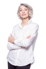 Happy trendy senior woman with a beautiful smile wearing a fashionable shirt standing with her arms crossed looking at the camera isolated on white background