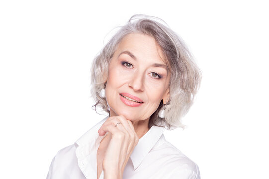 Close up portrait of pleasant grey-haired middle aged female resting her chin on a fist, looking at camera with a wide smile and showing happiness, isolated on white studio background