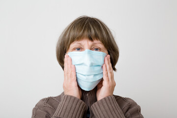 Old mature woman hands touching respirator mask on face for mouth and nose covering. Isolated on light gray background. Head closeup. First protection in virus time. Healthcare concept. Front view.