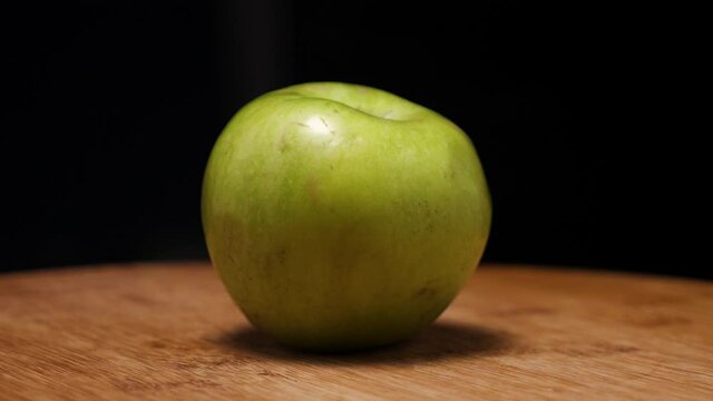 A green ripe apple on a wooden background. The camera flies around. Parallax effect. An apple of the renet simirenko variety. Close-up