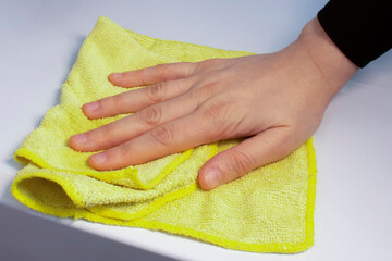 Female hand holding yellow microfiber cleaning cloth on white