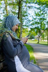 Profile view of the muslim pregnant woman using mobile phone and sitting alone in the park