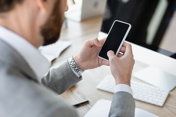 Cropped view of businessman using smartphone with blank screen in office.