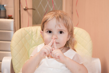A little two-year-old girl sits on a highchair and shows that she is 2 years old
