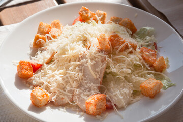 Appetizing caesar salad with bacon, croutons and cheese on a white plate in a restaurant