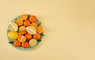 Plate of fresh juicy fruits tangerines and lemons on a yellow background. Vitamins and minerals, healthy eating.