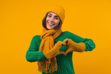 Studio portrait of beautiful smiling young woman in cozy warm knitted outfit is making heart sign with her hands
