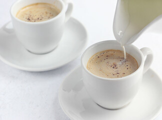 Cream is poured into coffee. There are two cups of coffee on the table.