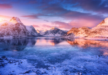 Aerial view of snowy mountains, blue sea with frosty coast, reflection in water, sky with pink...