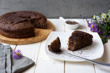 Sweet dessert: a piece of chocolate cake on a white plate and a chocolate cake on a white table. Close-up