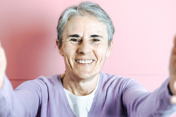 Old senior white hair woman holding the camera taking a selfie colourful background. Old people...