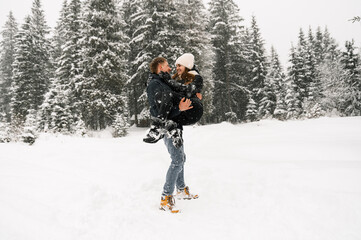 Fototapeta na wymiar Loving couple cuddling on a winter walk. Young family having fun in the frosty forest. Romantic date in winter time. Winter lovestory